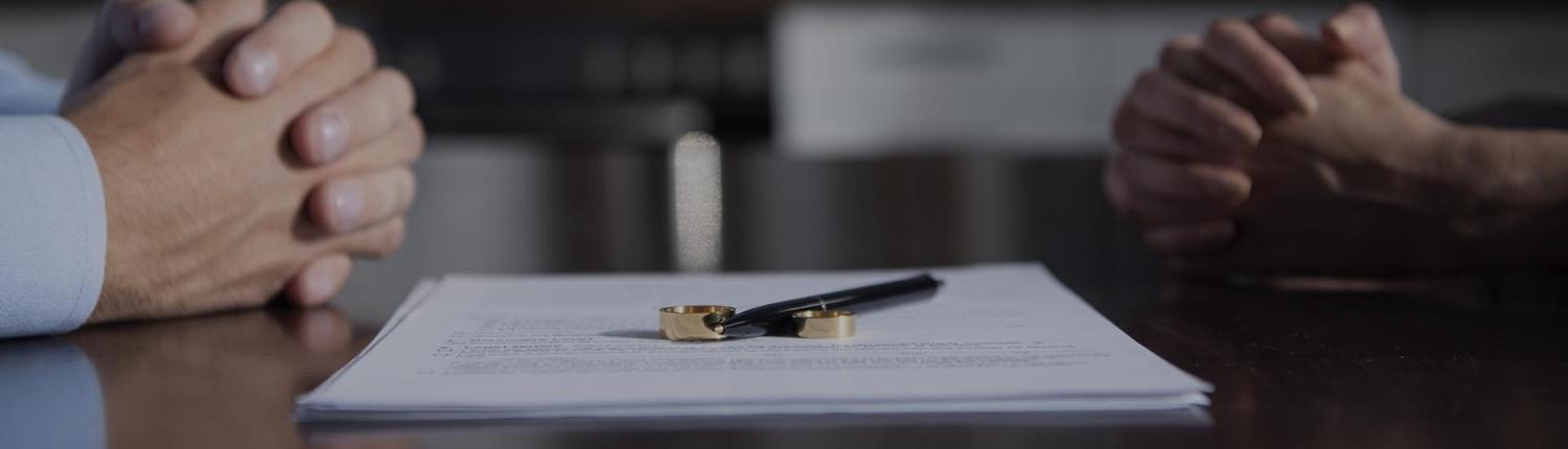 partial view of couple sitting at table with clenched hands near divorce documents